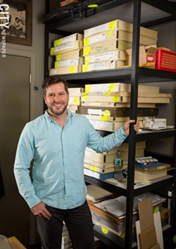 Adam Werth, in front of the boxed print collection of the Print Club of Rochester. - PHOTO BY JOHN SCHLIA