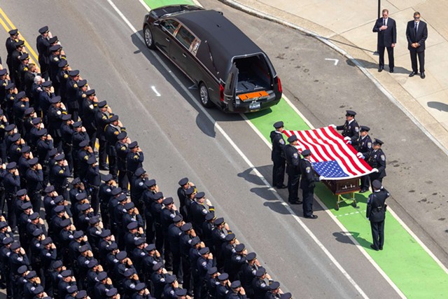 Police officers salute Officer Anthony Mazurkiewicz as pallbearers fold the flag that draped his casket. - PHOTO BY LAUREN PETRACCA