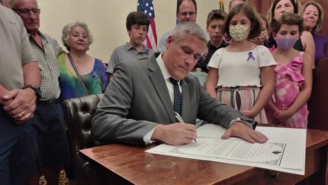 County Executive Adam Bello, surrounded by family of Carrie Ray, signs "Carrie's Law," which will mandate drivers to pass cyclists with at least three feet of space.